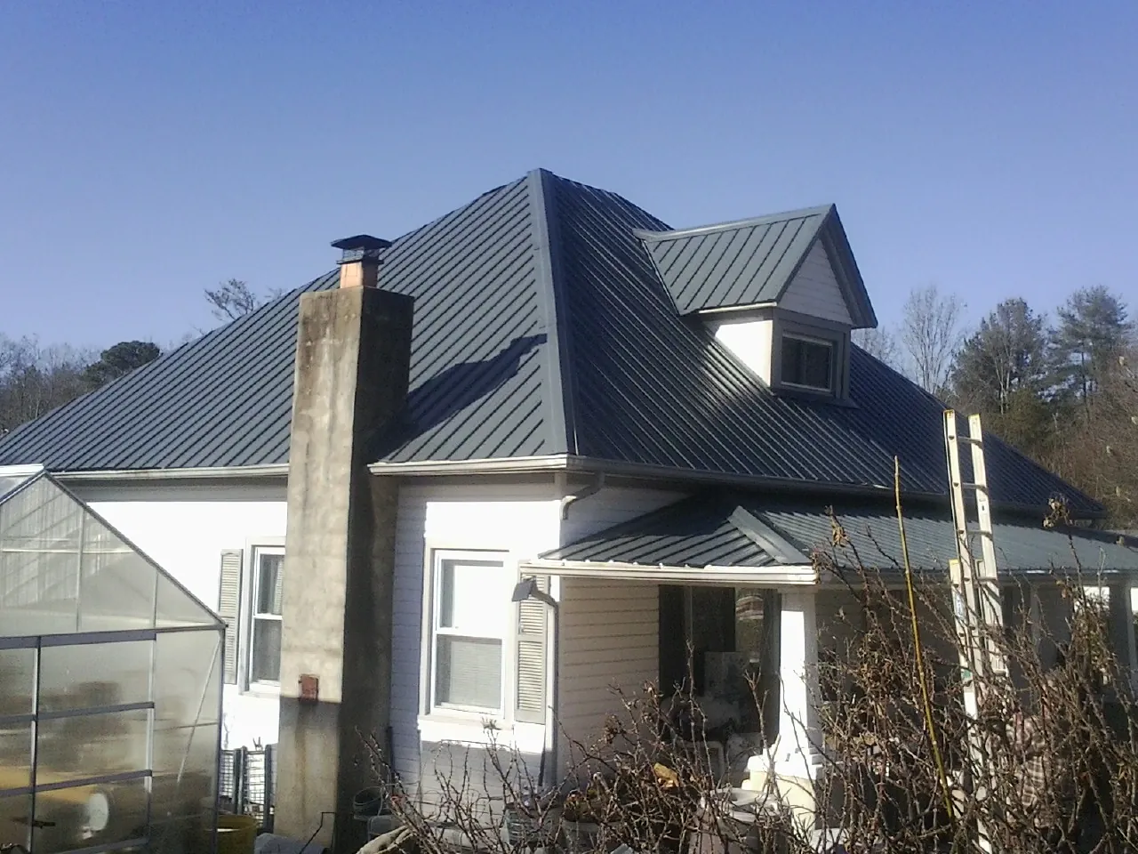 Dark blue standing seam metal roof on a white farmhouse with dormer — Slate & Tile Roof Repair by Roofing Brothers in Country Club Hills
