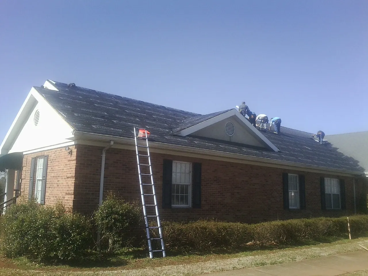 Crew tearing shingles off a brick ranch roof with a ladder set — Emergency Roof Repair work by our crew in Country Club Hills