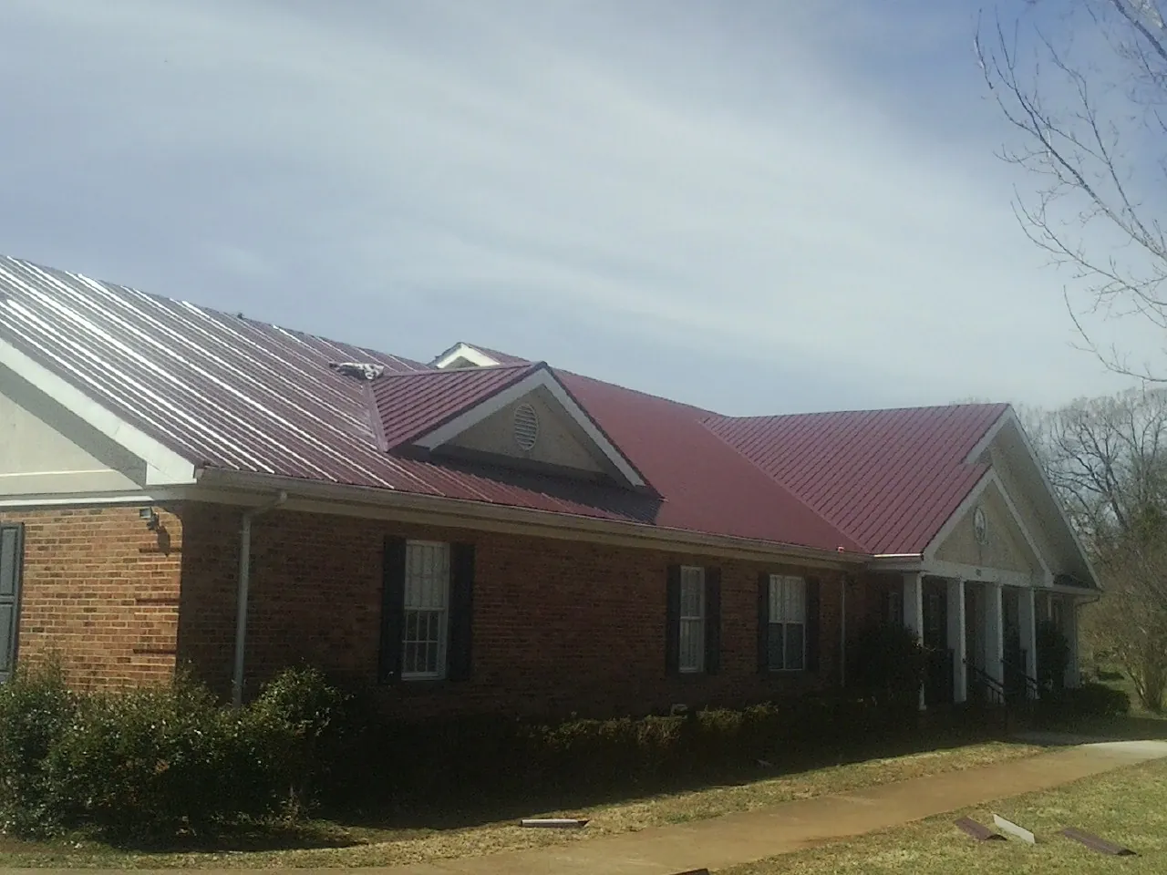 Red metal roof with gabled entries on a long brick building, from a Hail Damage Roof Repair job in Country Club Hills