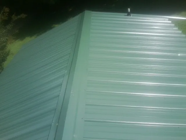 New green metal panels meeting at the ridge of a roof — Flat Roof Repair work by our crew in Country Club Hills