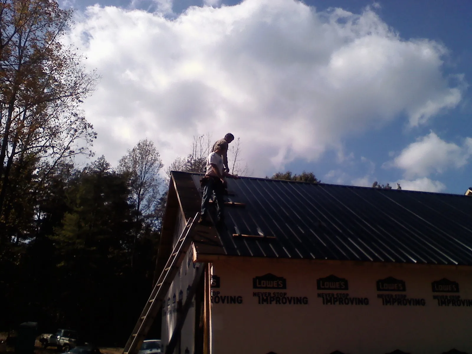 Roofer fastening dark metal panels high against a cloudy sky, from a Roof Inspection job in Country Club Hills