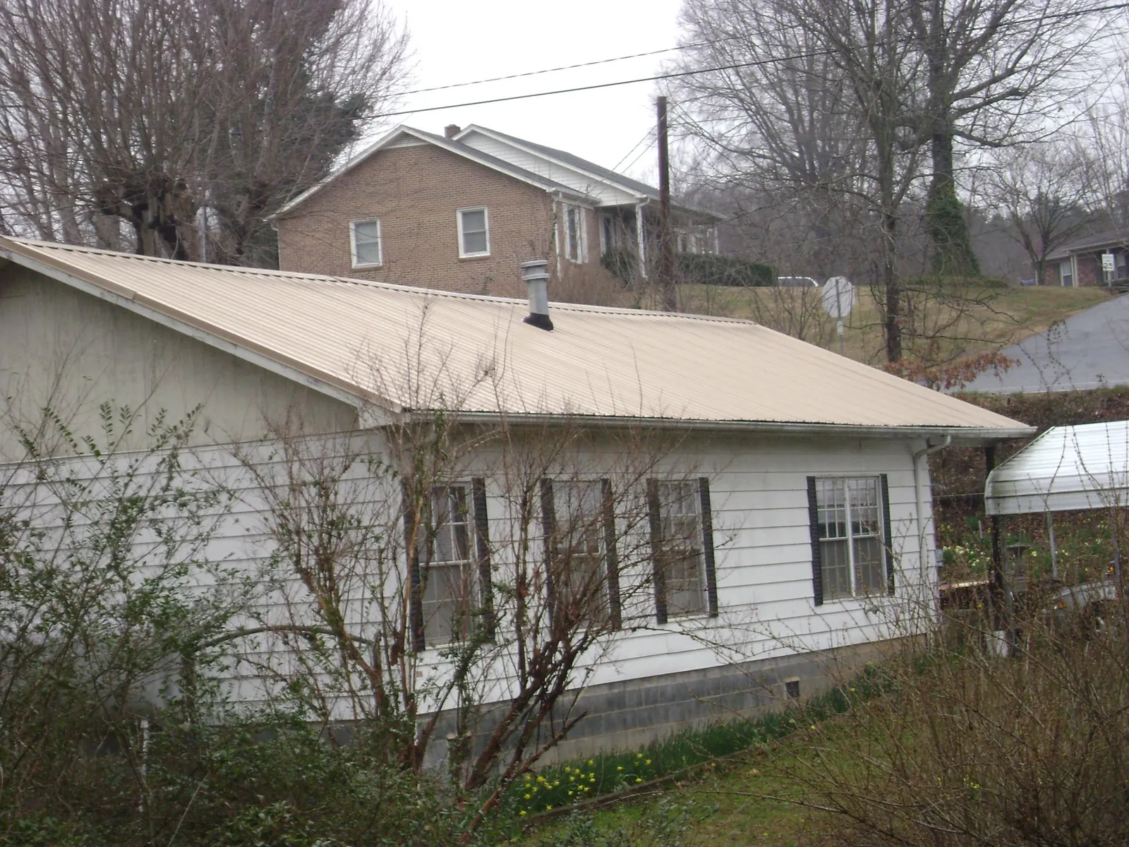 Tan metal roof on a white sided house set into a hillside — Commercial Roofing by Roofing Brothers in Country Club Hills