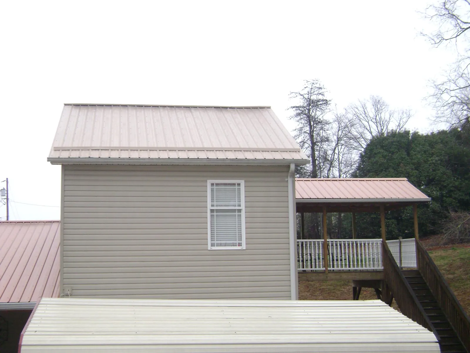Tan metal roofs on a two story addition and attached porch, from a Roof Replacement job in Country Club Hills